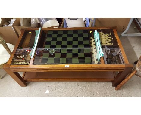 A teak and glass top two tier games table with contents of Cribbage board; Dominoes; chess pieces etc.