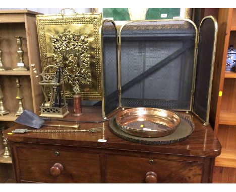 A quantity of brass and copper ware to include an embossed firescreen; a folding spark guard; trays; fire irons etc.