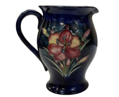 MOORCROFT; a tube lined pottery jug, decorated with the 'African Lily' pattern on a blue ground, height 15cm, impressed facto