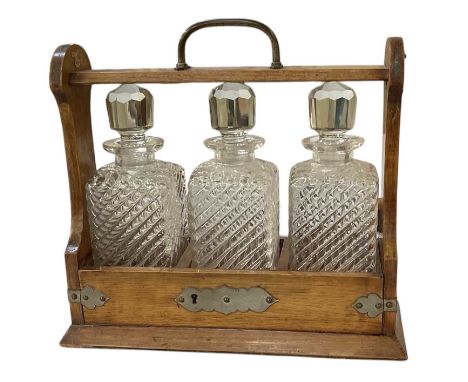 An early 20th century oak tantalus with silver plated mounts, with three cut glass decanters, height 33cm, width 33cm.