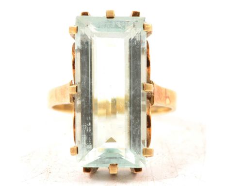 An aquamarine dress ring, the rectangular step cut stone, 21 x 9.7 x 6.3mm claw set in an all yellow metal mount, ring size a