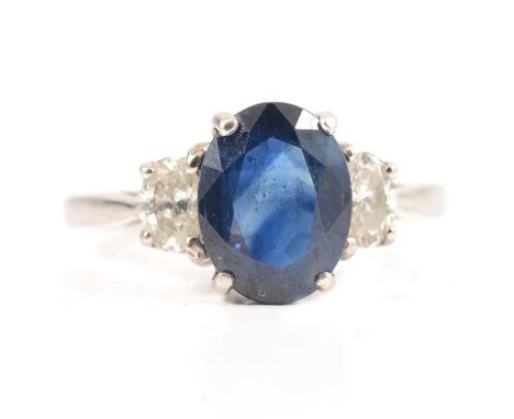 A sapphire and diamond three stone ring, the oval mixed cut sapphire 10.5mm x 7.5mm four claw set in an all white metal mount