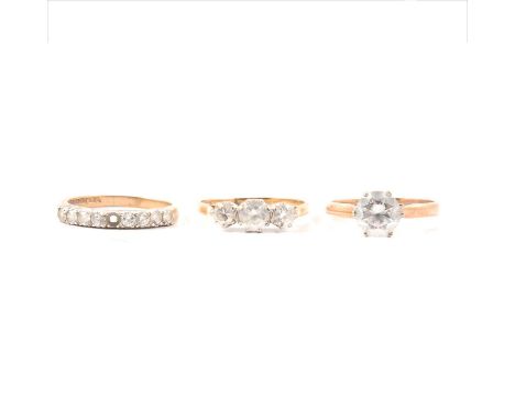 Three rings set with synthetic white stones, an 8mm diameter solitaire, a three stone ring, an eternity ring (one stone missi