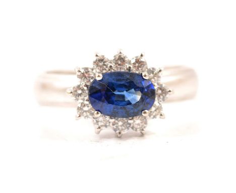 A sapphire and diamond oval cluster ring, the oval faceted sapphire claw set and surrounded by twelve brilliant cut diamonds 