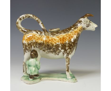 A late 18th/early 19thC prattware Cow Creamer, decorated in ochre and umber slip modelled with a figure milking the cow, H 13
