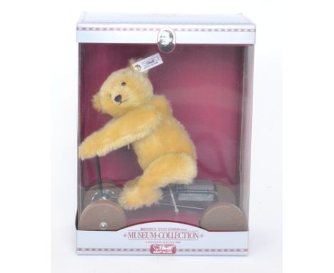 A modern Steiff limited edition teddy bear riding on a four wheeled trike, in display case with outer cardboard case.