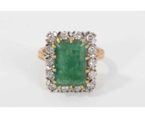 Emerald and diamond cluster ring with a rectangular step cut emerald measuring approximately 12.85mm x 8.75mm x 5mm, surround