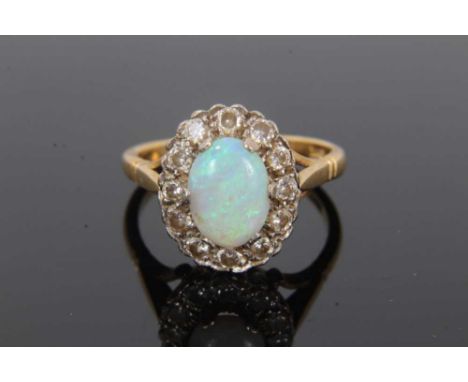 Opal and diamond cluster ring with an oval cabochon opal measuring approximately 8.9mm x 6.4mm x 2.1mm, surrounded by a borde