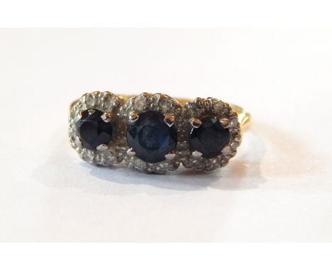 A diamond and sapphire half-hoop ring set three facet-cut sapphires, each having surround of tiny diamonds 