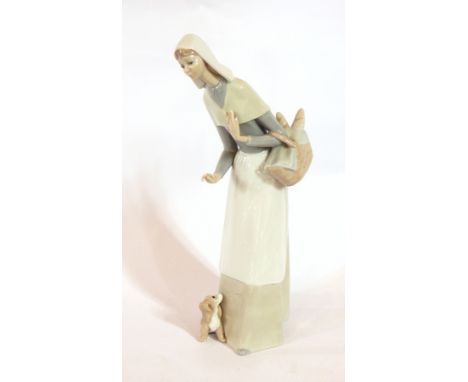 A Lladro figure of a woman wearing a wimple, carrying a basket of bread with a puppy at her feet, 27cm high 