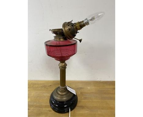 An early 20thc oil lamp with cranberry glass reservoir later converted to electricity, measures 50cm high
