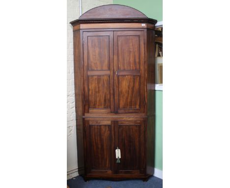 A REGENCY MAHOGANY FLOOR STANDING CORNER CUPBOARD in two sections with arching boxwood and ebony strung cornice over the twin