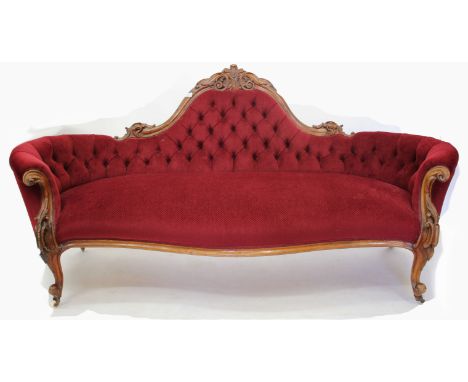 A VICTORIAN WALNUT FRAMED SOFA the shaped back with carved cresting rail, curved button upholstered arms and carved arm front