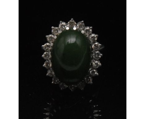 A Nephrite and diamond cluster ring, central oval nephrite cabochon  18.1 x  12.95 x 7.2mm, surrounded by a band of twenty ro