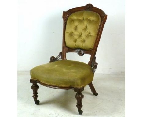 A Victorian walnut framed nursing chair, with green velvet button back and over stuffed upholstery, raised on carved and flut