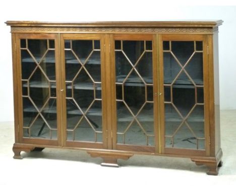 An Edwardian Chippendale style mahogany glazed bookcase with a blind fretwork frieze above four doors, enclosing shelves, rai
