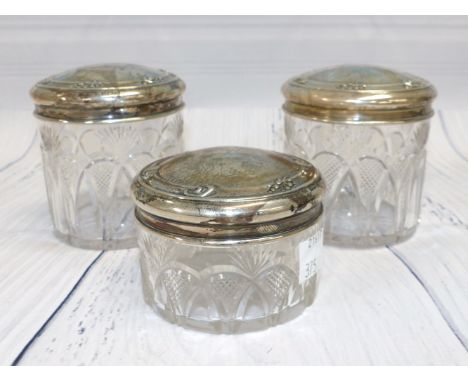 A pair of hallmarked silver top trinket jars and a smaller matching jar, Birmingham