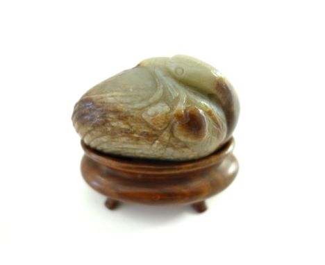 A Chinese celadon and russet jade bird, probably 17th century, carved with its head turned across its body and holding  a bra