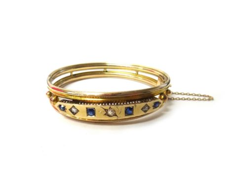 A sapphire and diamond set oval hinged bangle, with the principle cushion shaped diamond mounted at the centre, between two p