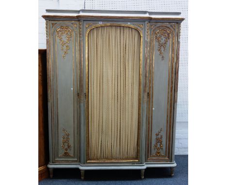 A Louis XVI style parcel gilt grey painted armoire, the breakfront central grill door flanked by smaller arch panel doors, on