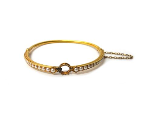 A gold and seed pearl set oval hinged bangle, (the central gemstone lacking), the shoulders mounted with rows of graduated se