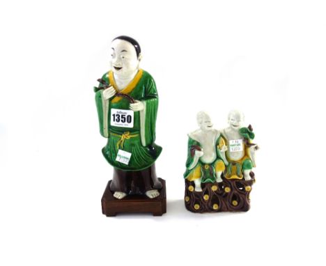 A Chinese famille-verte biscuit figure of a man, probably Kangxi, standing holding lotus flowers, 22cm.high, wood stand; and 