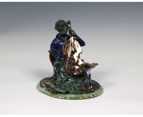 in green, blue and brown glazes, modelled sitting on a chair with scroll back and having a music stand, raised on oval base, 