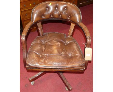 A contemporary mahogany and tan leather buttoned and brass studded swivel desk tub chair, with squab cushion, raised on rolle