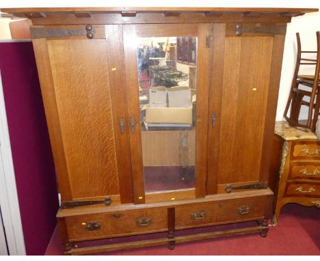 A Heal &amp; Sons Arts &amp; Crafts oak triple wardrobe, with proud overhanging cornice, above mirrored central door flanked 