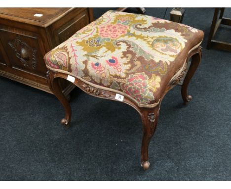 A mahogany effect footstool with carved decoration, claw and ball feet with a woven tapestry seat.