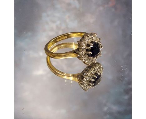 An 18ct gold sapphire &amp; diamond cluster ring, the central oval sapphire meas. 6 x 5mm within a border of ten round diamon