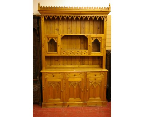 A REPRODUCTION PINE GOTHIC OAK STYLE DRESSER, the castellated top over a decorative canopy frieze, open top shelf and central