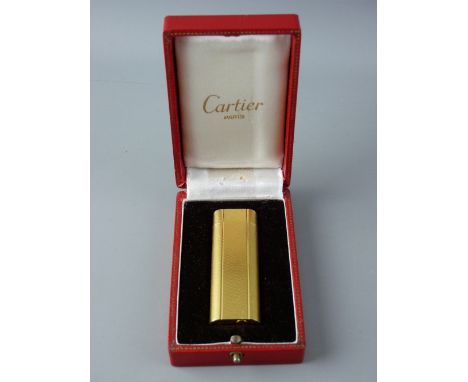A CASED CARTIER YELLOW METAL CIGARETTE LIGHTER, no. A21161 and with neat hard cover Cartier instruction booklet