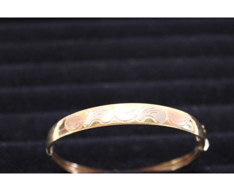 A solid 18ct gold bangle with a two tone gold leaf decoration. 14.42 grams. 