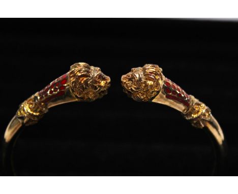 A 14ct gold bangle with Lion head finials &amp; red enamelling. 28.22 grams (small steel spring) 