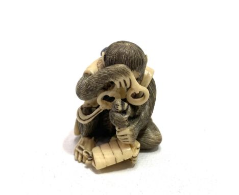 A good Japanese Meiji period ivory netsuke carved as a seated monkey holding spectacles, looking at a netsuke on an Inro, sig