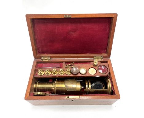 An early 20th century brass lacquered microscope with various accessories within a fitted mahogany hinge lidded box with pink