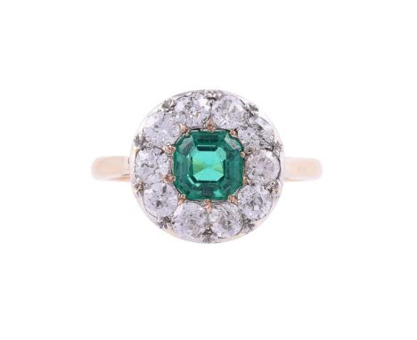 AN EMERALD AND DIAMOND CLUSTER RINGThe step cut emerald with canted corners within a surround of old brilliant cut diamonds, 