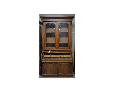 A Victorian mahogany cylinder bureau bookcase, the ogee cornice above a pair of arched glazed panel doors enclosing adjustabl