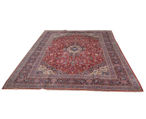 A Kashan carpet, the floral medallion surrounded by foliate scrolls on a red ground, 410 x 300cms.