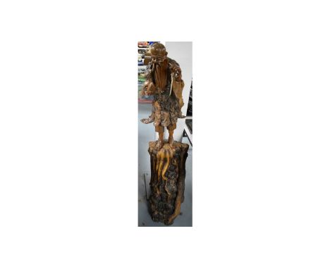 A Chinese carved root wood figure, modelled standing, upon a naturalistic tree trunk base, 135cms high.