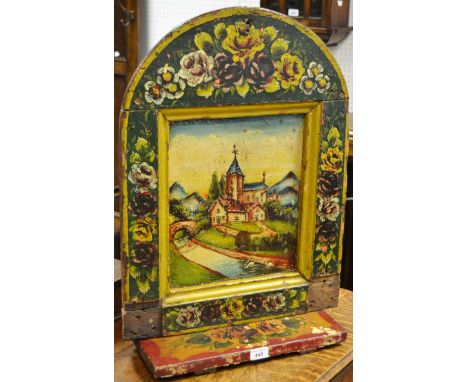 A painted wall plaque, arched top,painted with alpine church scene, shelf to bottom.