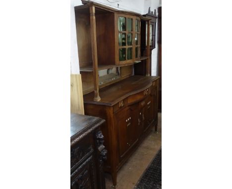 An Arts and Crafts oak dresser with green glazed cupboard doors, base fitted with bow-front frieze drawer, and stylised inlai