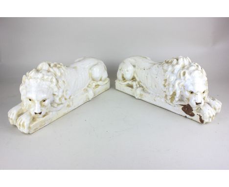 A pair of ceramic lion figures, reclining with heads turned, 31cm