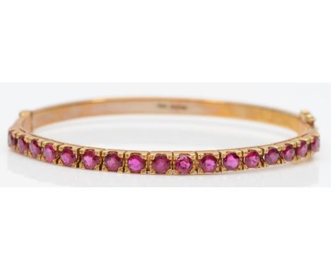 A 9ct gold and ruby hinged bangle, Birmingham 1986, claw set with 17 brilliant cut stones, internal 58 x 49mm, 14.6gmIn very 