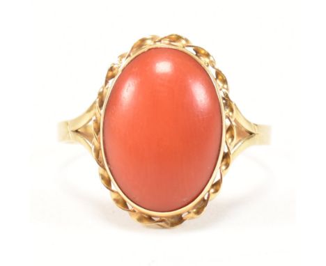 An 18ct gold and coral ring. The ring set with a single coral cabochon in a twisted edge mount with split shoulders to plain 