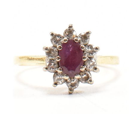 A hallmarked 18ct gold, diamond and ruby cluster ring. The ring having a central oval cut ruby flanked by a halo of ten round