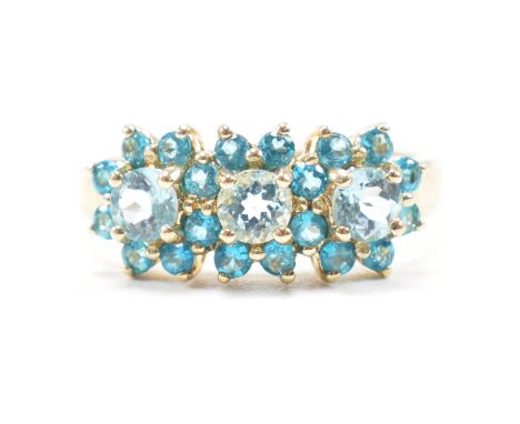 A hallmarked 9ct yellow gold and topaz cluster ring. The ring having three floral clusters comprised of pale and vibrant blue