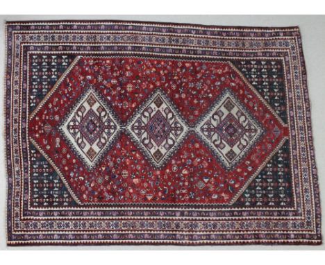 A hand woven Persian wool carpet with red ground, three cream diamond medallions, field decorated stylized floral motifs, mul