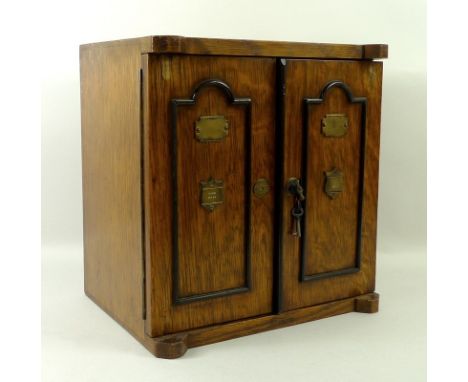 An oak smoker's cabinet, early 20th century, the two doors with beaded decoration and brass escutcheons opening to reveal two